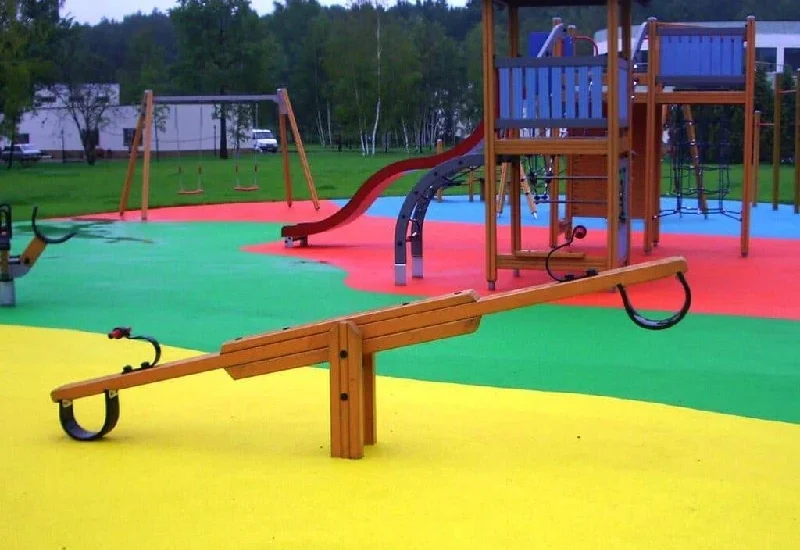 Colorful children's playground with a wooden seesaw in the foreground, installed on an EPDM rubber flooring surface. Colorful children's playground with a wooden seesaw in the foreground, installed on an EPDM rubber flooring surface.