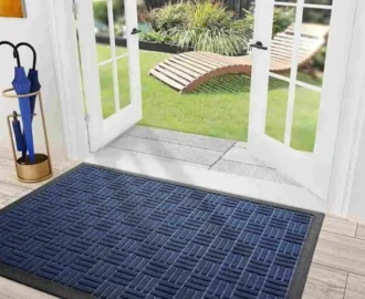 An eye-level shot captures a dark blue and black textured waterhog mat lying on a light wood floor just inside a set of open white French door. An eye-level shot captures a dark blue and black textured waterhog mat lying on a light wood floor just inside a set of open white French door.