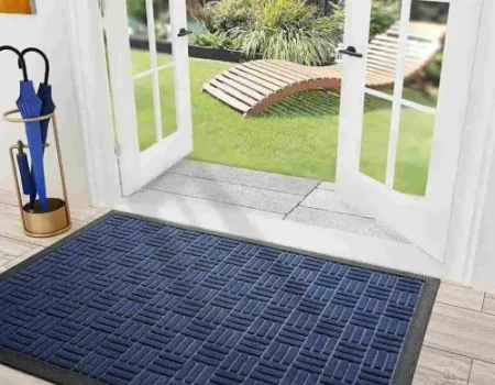 An eye-level shot captures a dark blue and black textured waterhog mat lying on a light wood floor just inside a set of open white French door. An eye-level shot captures a dark blue and black textured waterhog mat lying on a light wood floor just inside a set of open white French door.